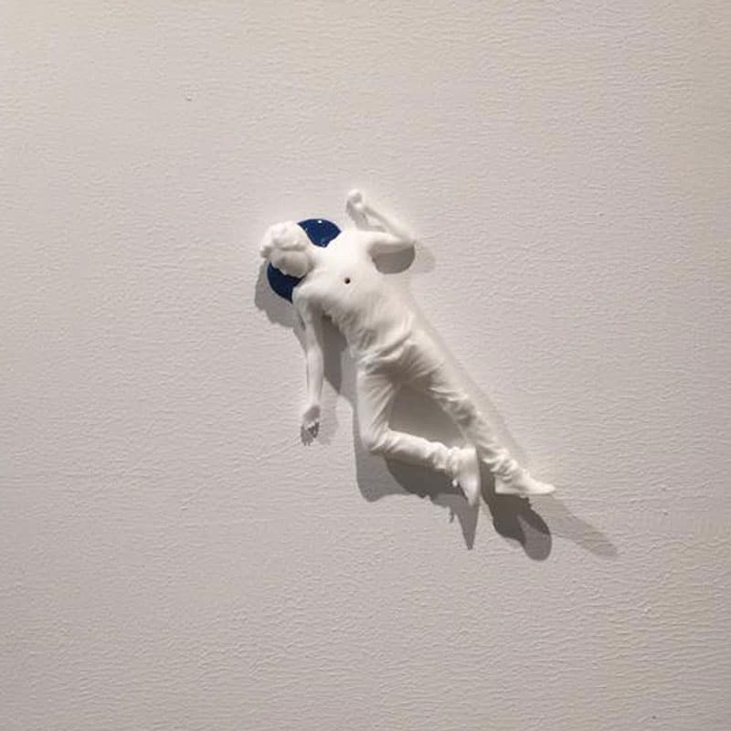 Blue Ego Death by Federico Clapis: a small white nylon powder figure sprawled on textured white canvas with a deep blue halo behind his head