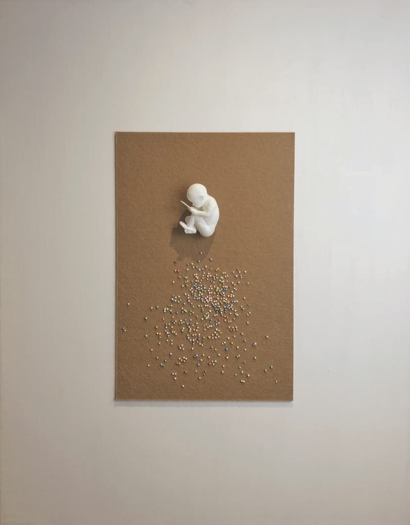 Chromosome by Federico Clapis on a white wall: a white fetus holding a phone on beige wool canvas above scattered coloured beads