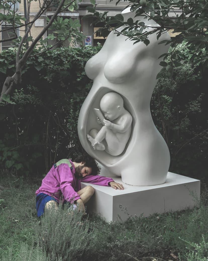 Side view of Connection by Federico Clapis: the fetus looks at a phone inside the white torso, the artist resting his head on the base