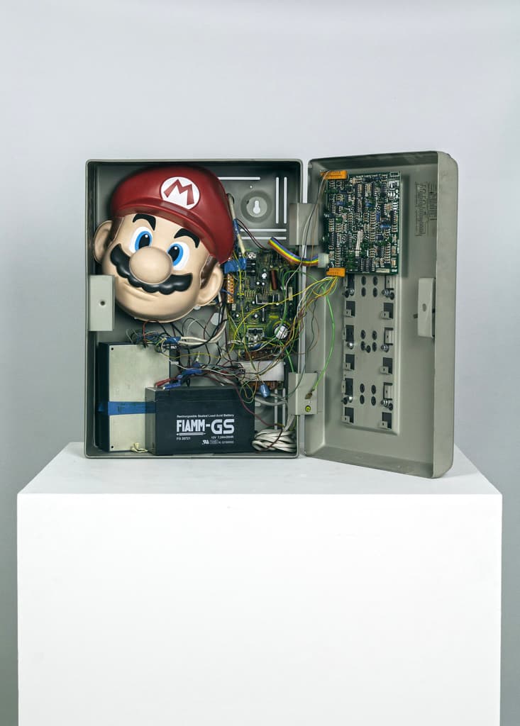 Digital Mask by Federico Clapis, open: Super Mario mask among circuit boards, wires and a battery inside a grey alarm panel