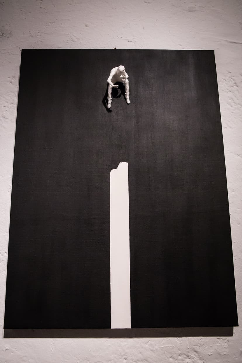 Fear Of Fusion by Federico Clapis, full view: black canvas on a white wall with a small crouching figure above a white vertical stripe
