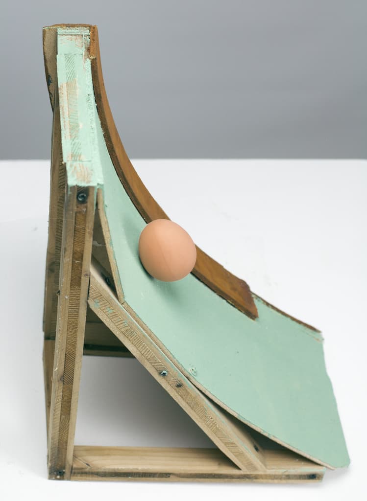 Side view of Life Factory by Federico Clapis, showing the wooden frame under the green curved ramp and the egg halfway down