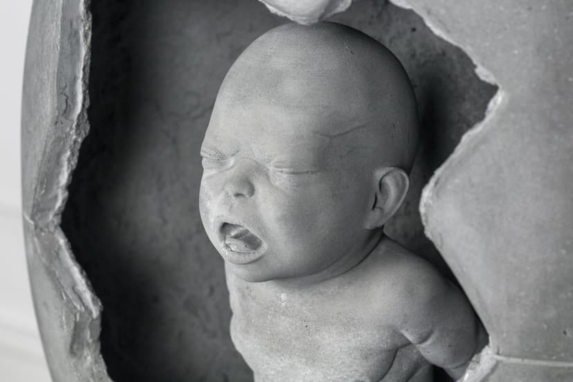 Mamaegotchi by Federico Clapis, close-up of the crying concrete baby's face with eyes shut and mouth open inside the cracked shell