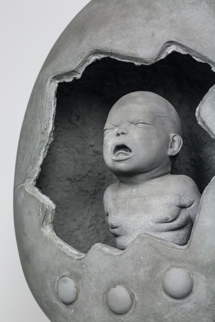 Mamaegotchi by Federico Clapis, angled detail of the screaming concrete newborn emerging from the broken egg above its three buttons