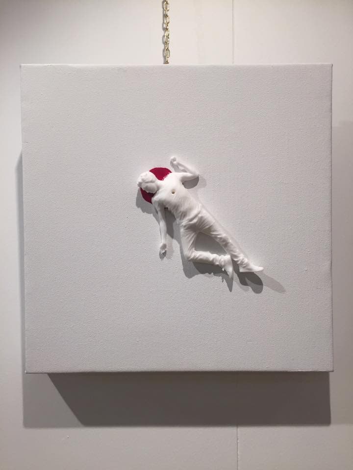Red Ego Death by Federico Clapis hanging on a wall: a small square white canvas with a lying white figure and a red circle