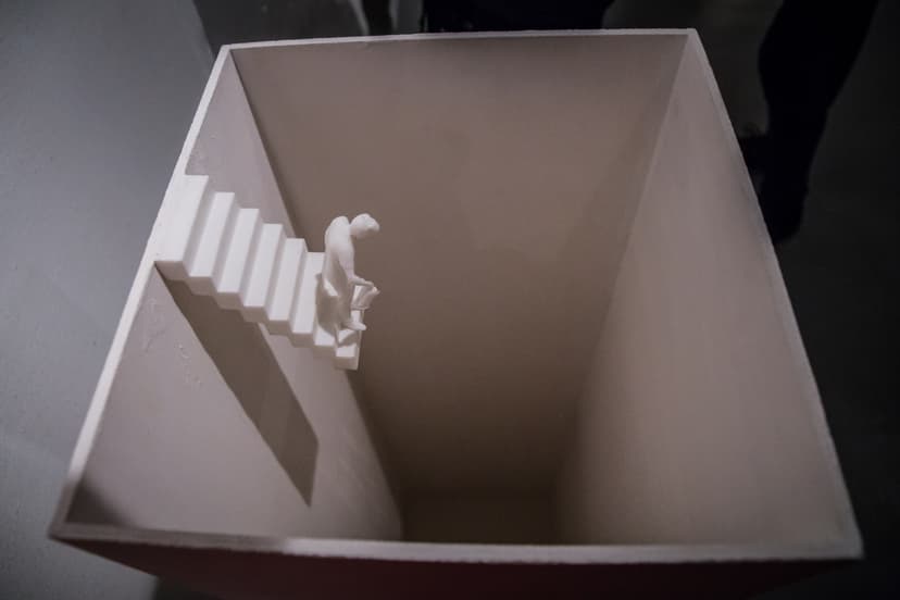 Relative Help by Federico Clapis seen from above: a small white figure walks down a staircase built into the wall of a deep white box