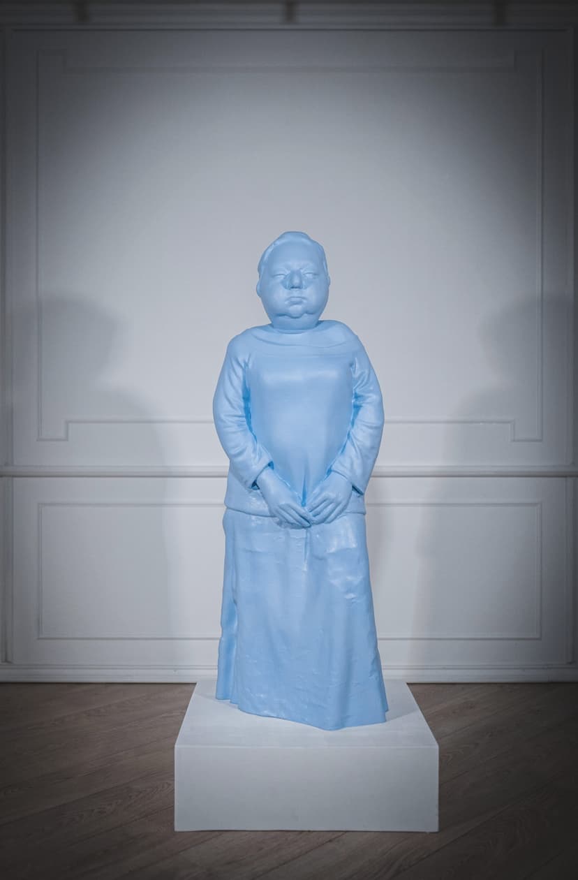 Taboo by Federico Clapis: light blue elastic polymer statue of a heavyset standing figure with clasped hands on a white plinth