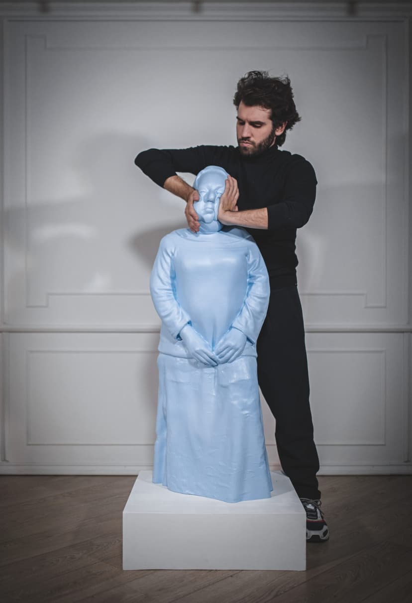 Federico Clapis in black squeezing the face of his sculpture Taboo, a light blue elastic polymer figure, with both hands