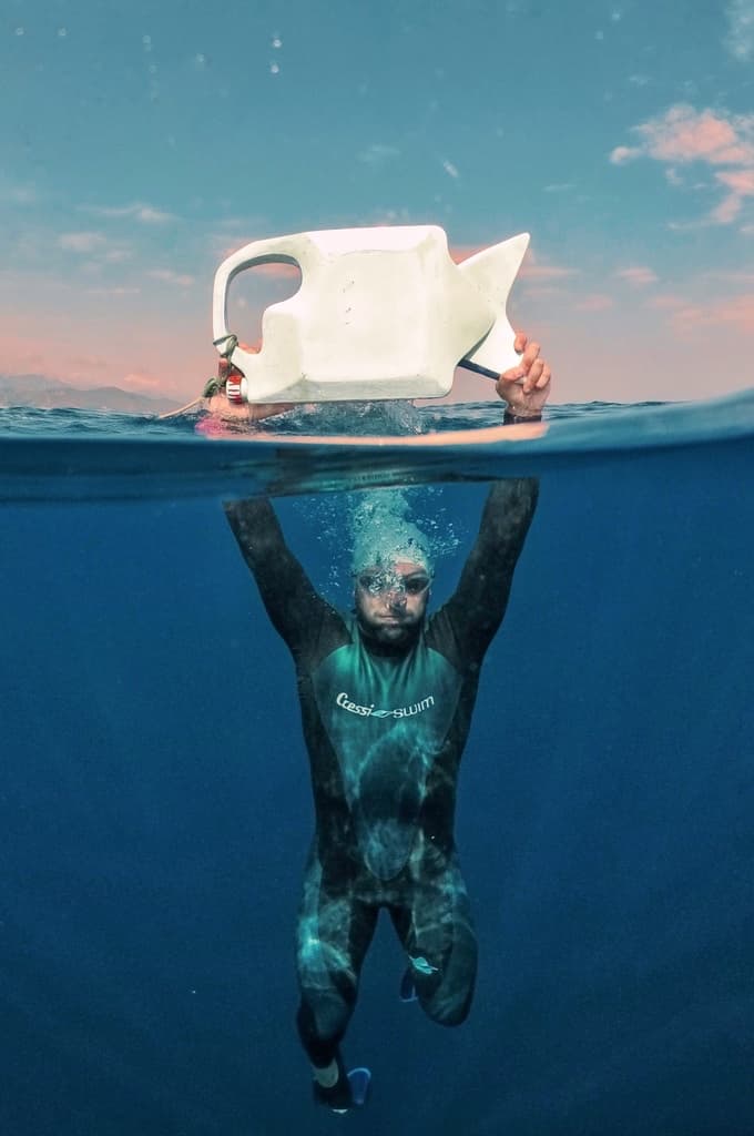 Tank Fish held above the sea surface by Federico Clapis in a wetsuit, split view above and below the water