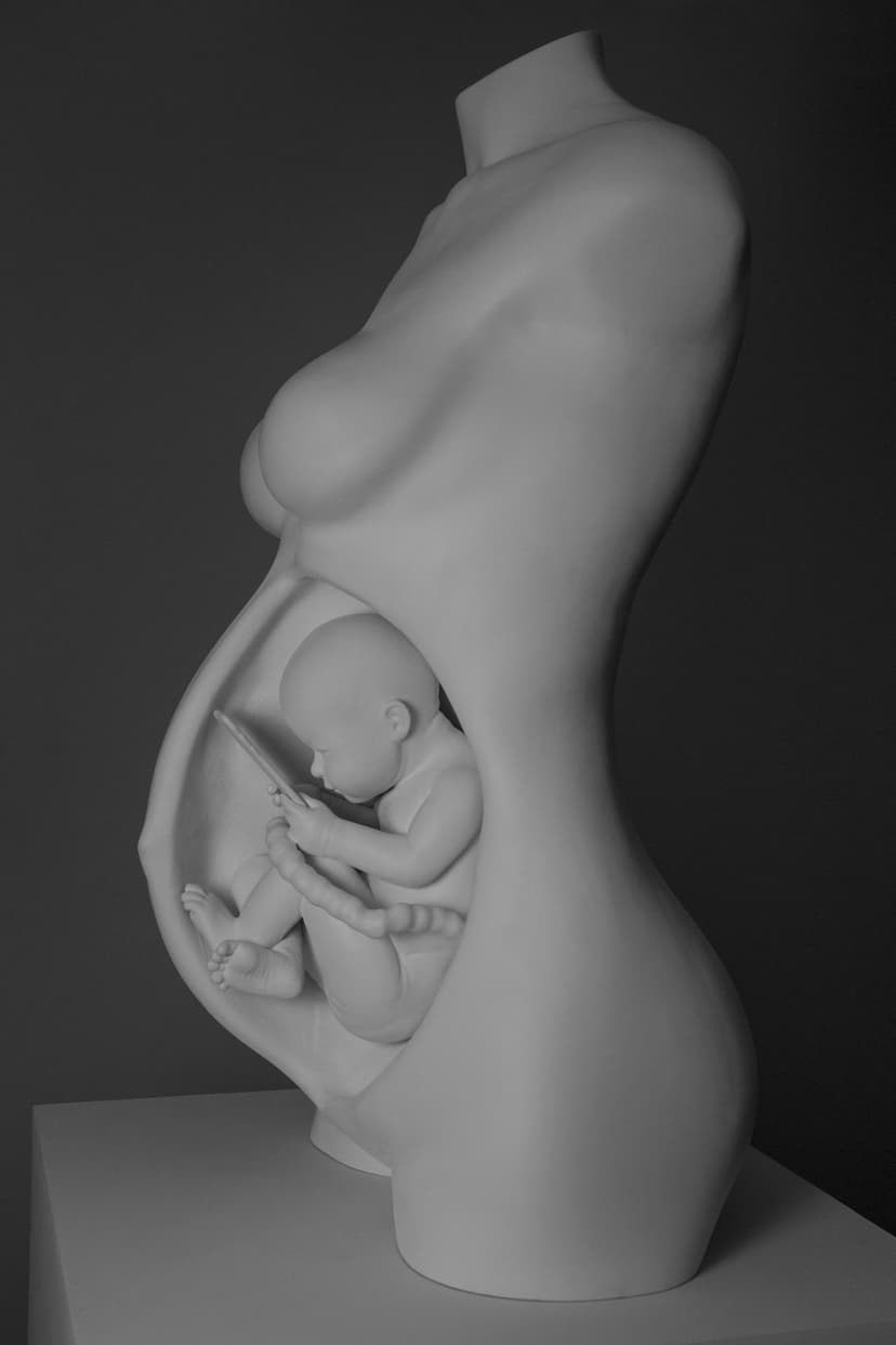 Side view of The Connection, a white resin sculpture by Federico Clapis: pregnant torso with a fetus inside gazing at a phone