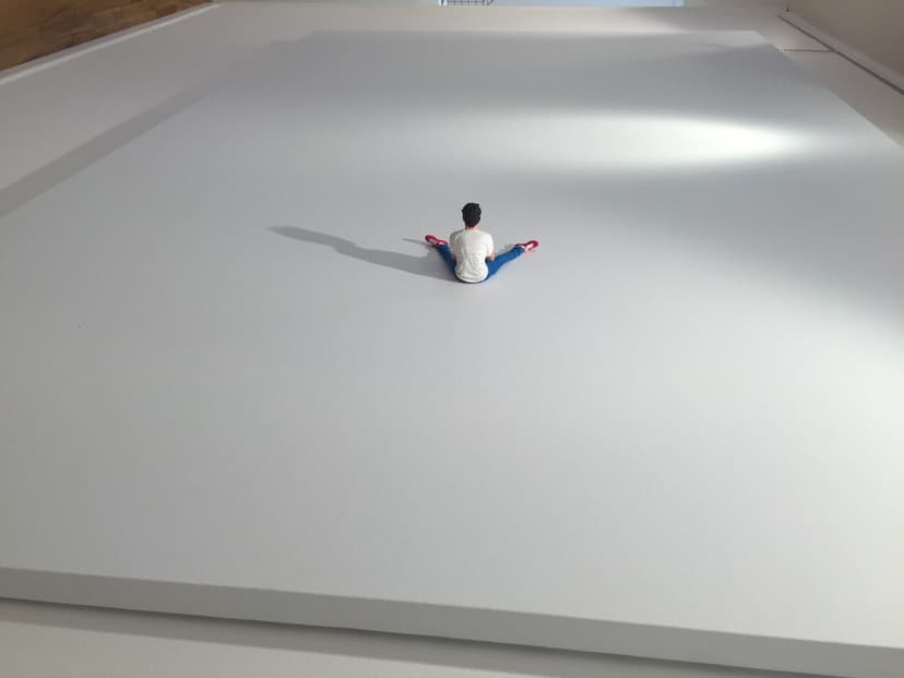 The Immense by Federico Clapis: small colour figure of a man in jeans sitting with legs apart on a vast white canvas, seen from behind