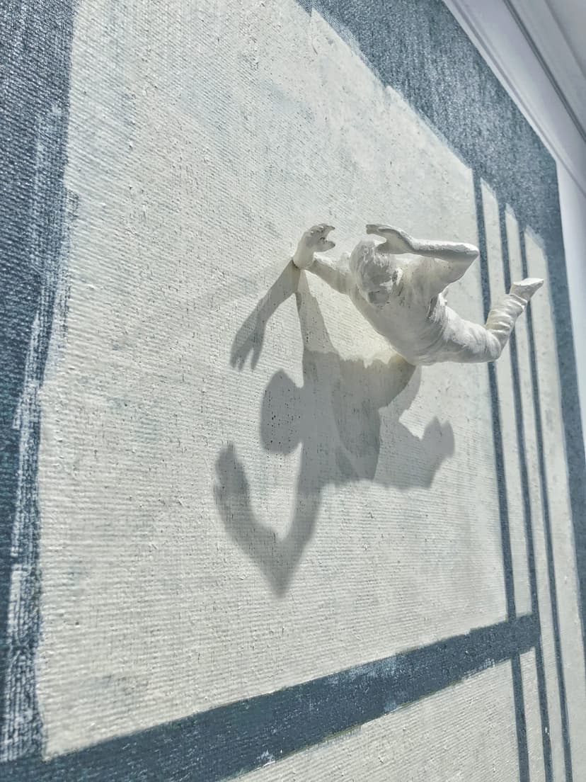 Angled close-up of Verticality by Federico Clapis: the falling white nylon figure and its sharp shadow on the cream painted canvas