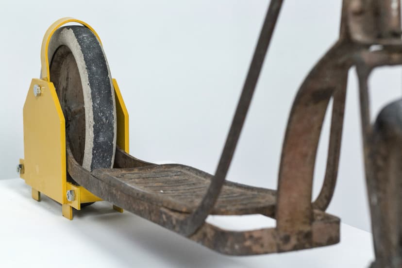 Detail of Violated by Federico Clapis: the worn footboard and rear wheel of the old iron scooter gripped by the yellow clamp