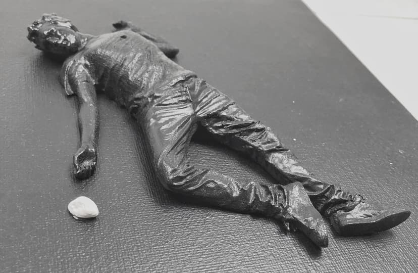 Low-angle detail of White stone by Federico Clapis: the lying black figure with arm stretched toward a small white pebble