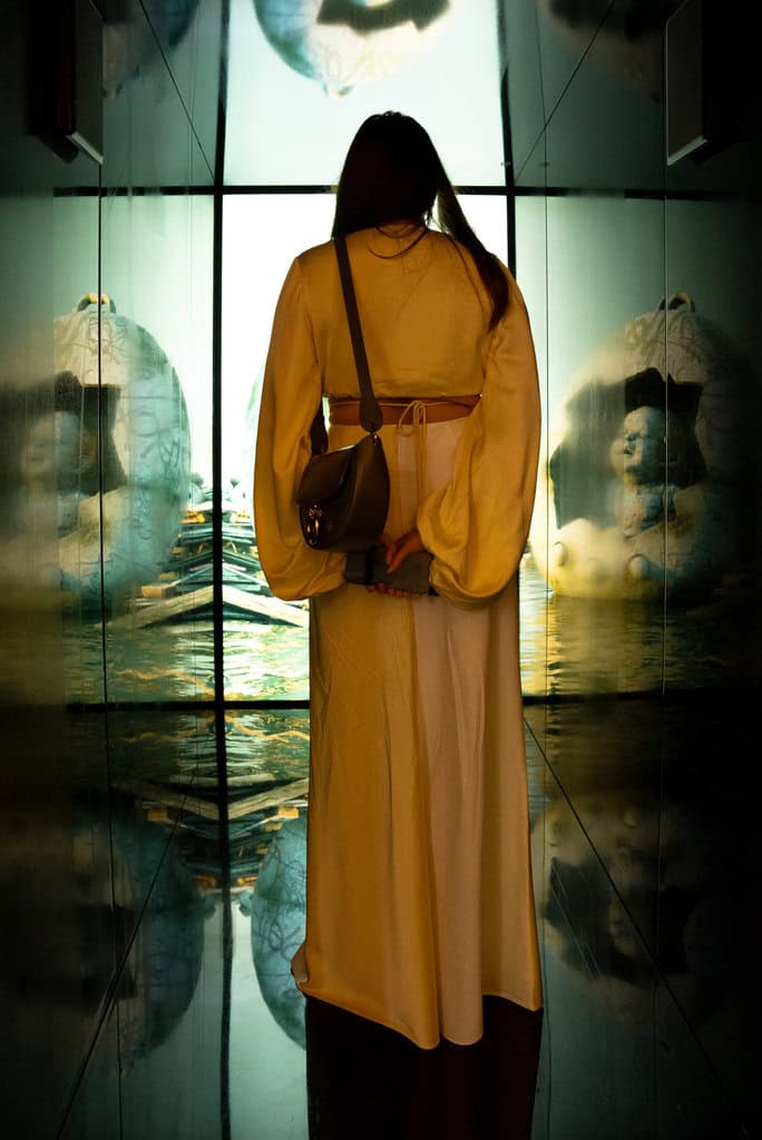 Visitor in a mirrored room at the Art In Space presentation at Art Dubai, facing a screen with reflected sculptural figures by Federico Clapis