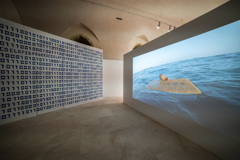 Contact Zone at EXMA Cagliari: a wall of binary code spelling Federico Clapis' name faces a video of a child adrift at sea on a doormat