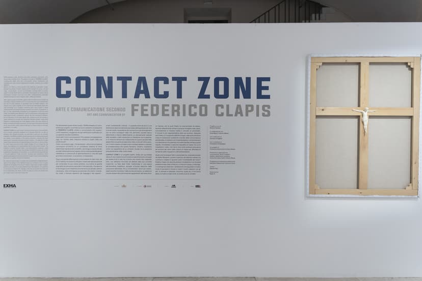 Title wall of Contact Zone, art and communication by Federico Clapis at EXMA, beside a bare canvas frame with a small crucified white figure