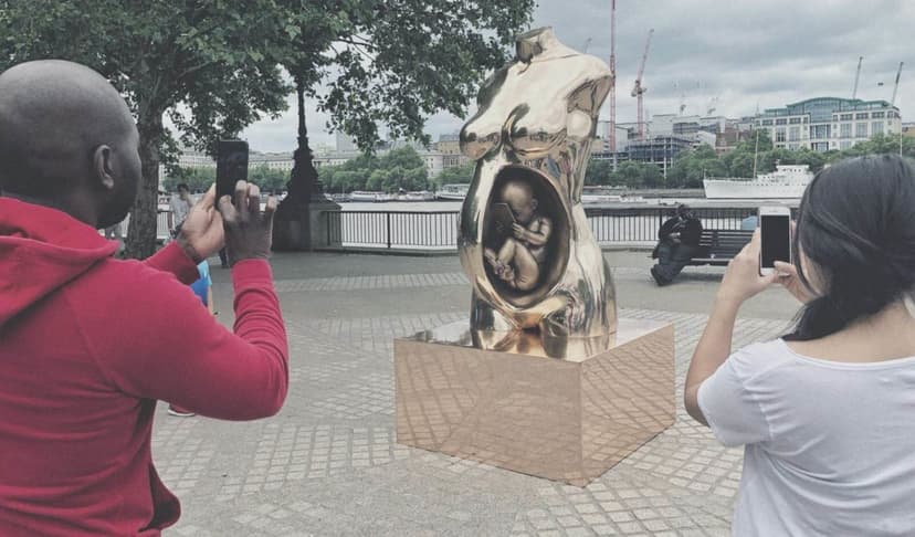 Visitors photograph Federico Clapis' Crypto Connection with their phones at Observation Point, London, the River Thames and cranes in the background