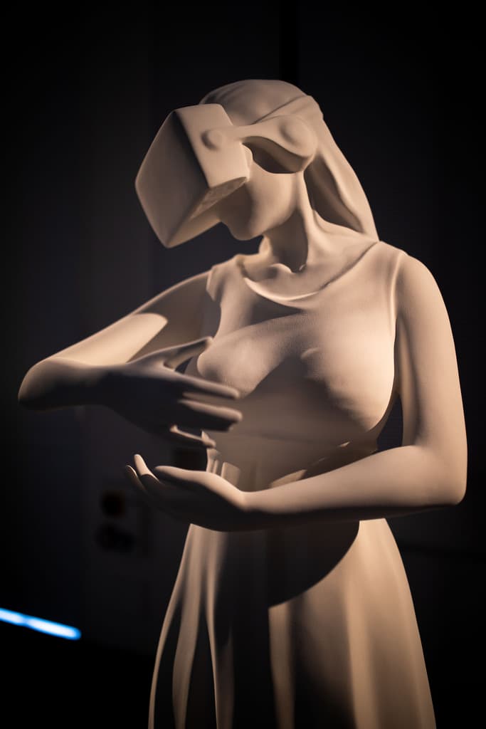 White sculpture by Federico Clapis of a woman wearing a VR headset and cradling the air, shown at the Deep Scrolling Experience in Milan