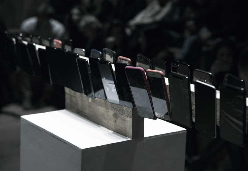 A long row of smartphones standing on a wooden support atop a white plinth, an installation by Federico Clapis at the Deep Scrolling Experience