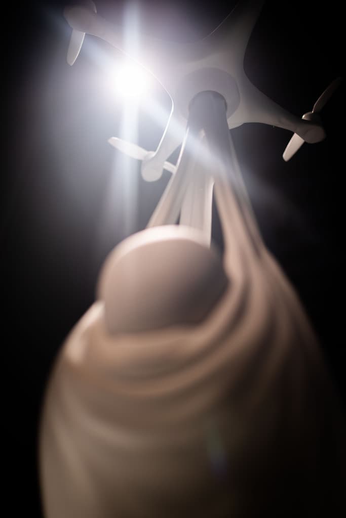 Close view of a white sculpture by Federico Clapis, a drone carrying a newborn in a sling, backlit by a spotlight at Triennale Milano