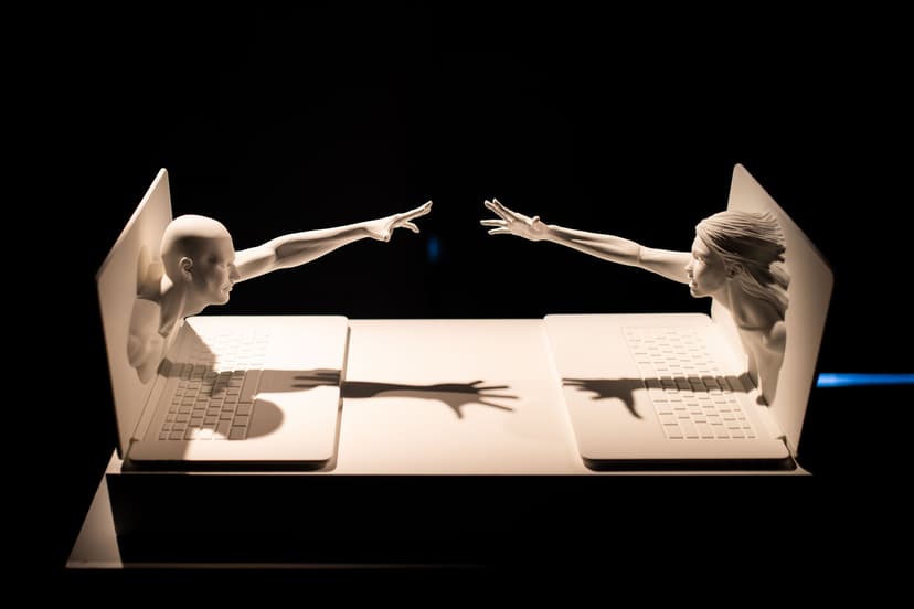Sculpture by Federico Clapis of a man and a woman leaning out of two laptops to touch hands, lit in the dark at the Deep Scrolling Experience