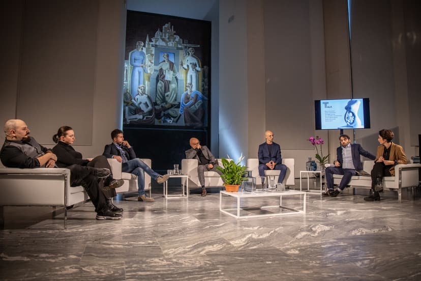 Panel of speakers on white sofas in a hall of Triennale Milano, with a screen and a large mural, during a talk of the Deep Scrolling Experience