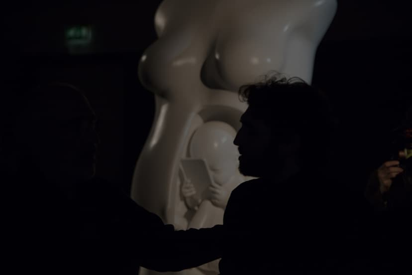 Federico Clapis in silhouette beside his white sculpture of a pregnant torso with a foetus holding a smartphone, at Triennale Milano
