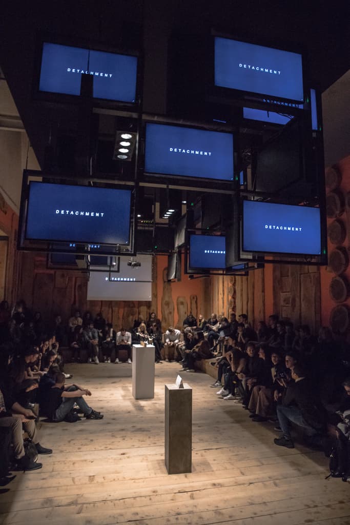 Seated visitors beneath suspended monitors showing the word Detachment, a video installation by Federico Clapis at the Deep Scrolling Experience