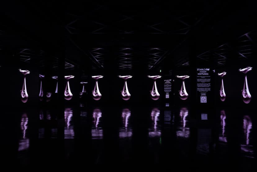 A row of tall screens showing Federico Clapis' animation of a drone carrying a pale bundle, in the dark hall of Disruption by W1 Curates, London