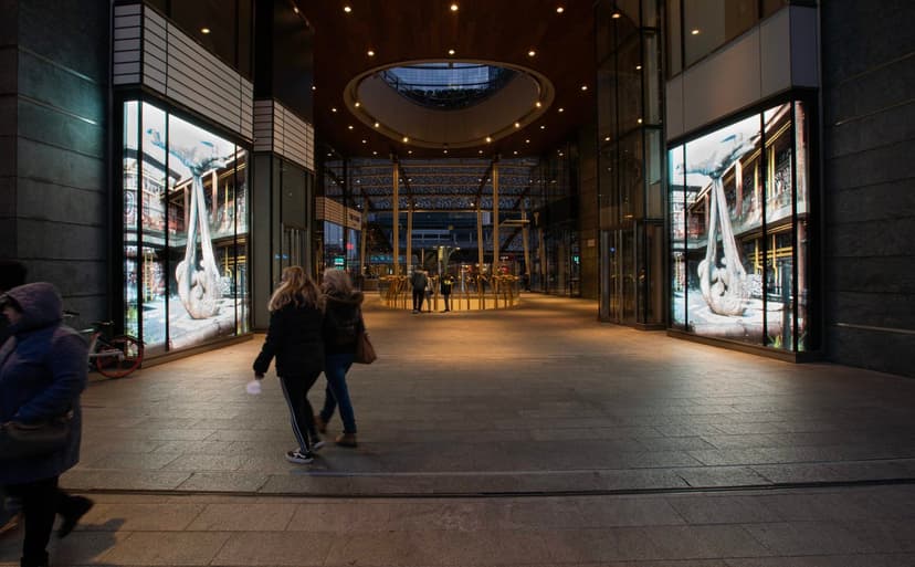 Visitors walk past glowing LED walls showing Federico Clapis's Concrete Babydrone in a passage of Piazza Gae Aulenti, Milan