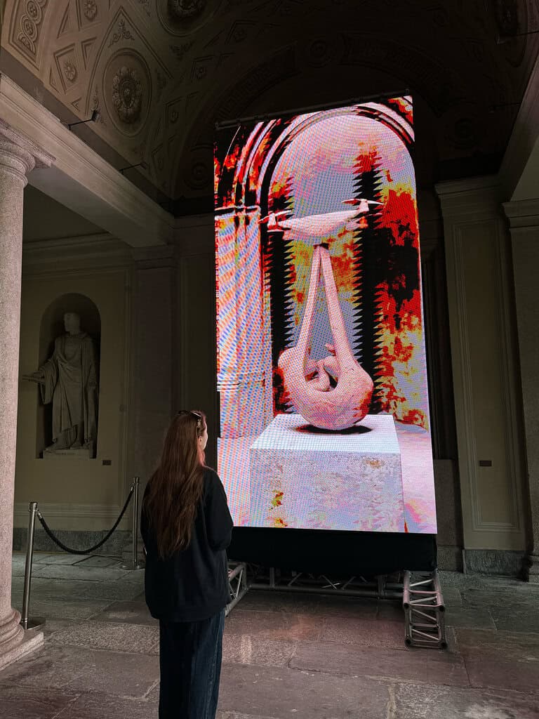 A visitor watches Federico Clapis' Babydrone, glitched in red and pink, on an LED wall under the vaults of Palazzo Civico at Lugano NFT Fest