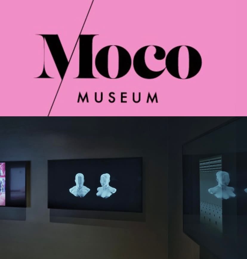 Moco Museum logo above a dark NFT room in Barcelona where screens show two faceless white busts, a digital sculpture by Federico Clapis
