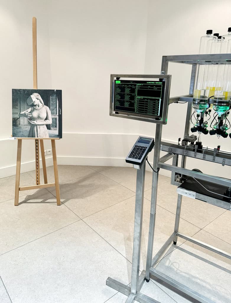 Print by Federico Clapis of a statue wearing a VR headset on a wooden easel, beside a machine with bottles and a monitor, at The Future of Art in Paris