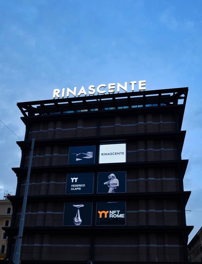 Facade of La Rinascente in Rome at dusk with screens showing Federico Clapis' name and his works for the NFT Rome Curated initiative