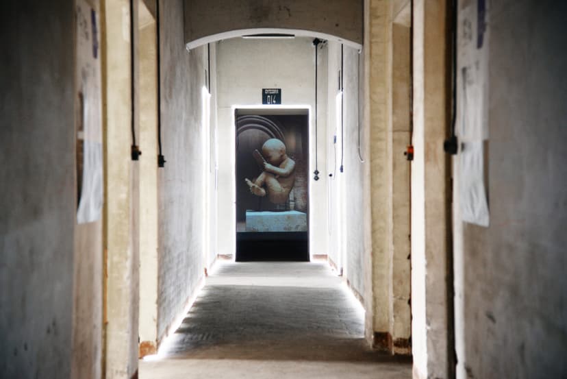 Long corridor of Scalo Vallino in Turin ending in a backlit screen with a digital sculpture of a foetus with a smartphone by Federico Clapis
