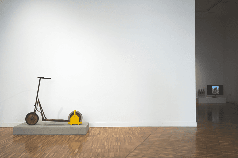 Old child's scooter with a yellow wheel clamp on a concrete base, a work by Federico Clapis at Bianchi Zardin Contemporary Art in Milan