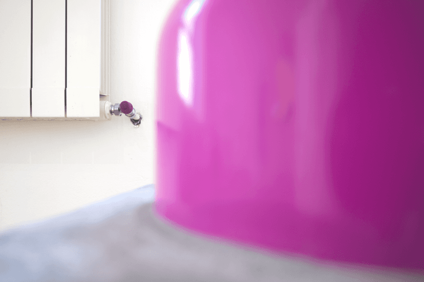 Close view of a glossy magenta gas canister on concrete beside a radiator valve, in Federico Clapis' exhibition at Bianchi Zardin, Milan