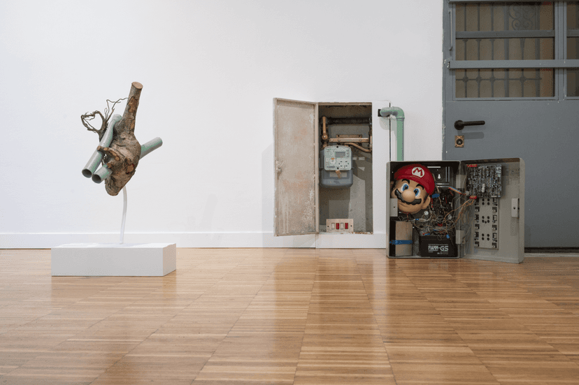 A tree branch fitted with green pipes, an open meter box and a Super Mario mask among wiring, works by Federico Clapis at Bianchi Zardin, Milan