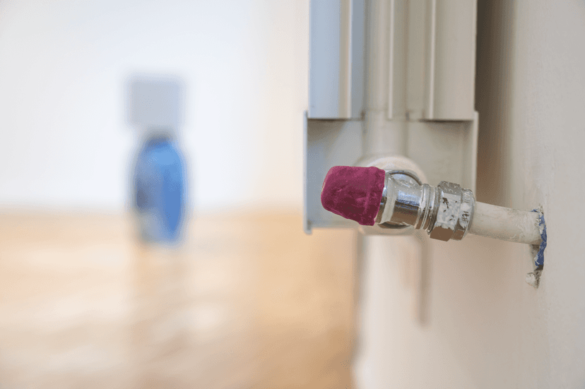 Radiator valve capped in red felt, with a vase blurred in the background, a detail of Spazio mentale = ambiente by Federico Clapis in Milan