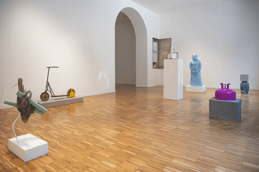 Gallery room with a clamped scooter, branch sculpture, blue figure and magenta canister, installation view of Federico Clapis at Bianchi Zardin