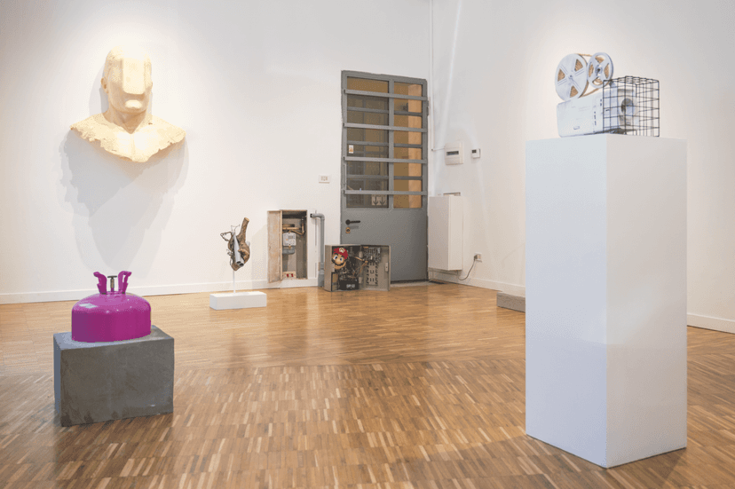 Wall-mounted cream bust, magenta canister, film projector on a plinth and open cabinets, installation view of Federico Clapis at Bianchi Zardin