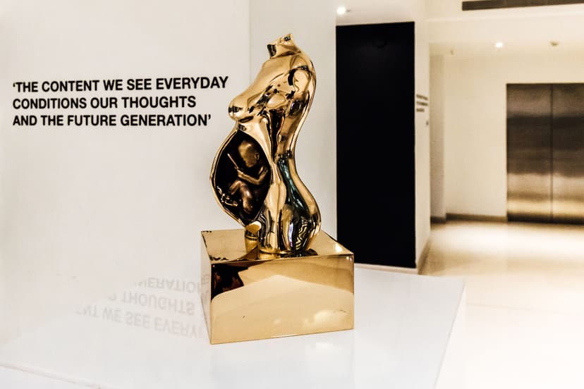 Gold sculpture by Federico Clapis of a pregnant torso with a fetus holding a smartphone, shown at Visual Diet in the M&C Saatchi London foyer